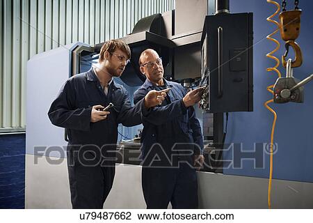 Stock Image - An experienced worker explains the workings of a CNC machine to an apprentice. Fotosearch