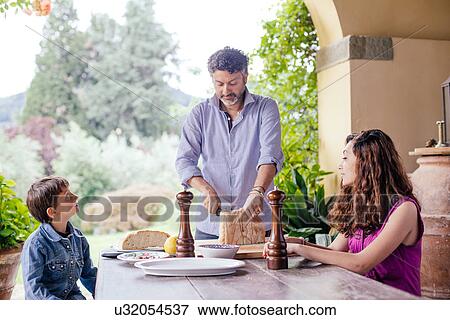 Stock Photo - Boy and girl waiting as father cuts bread. Fotosearch