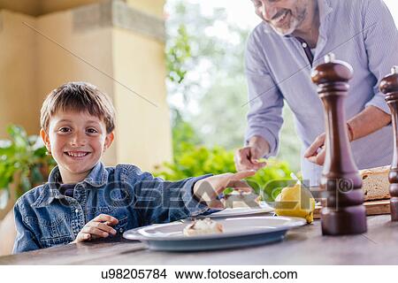 Picture - Boy at table whilst father prepares food. Fotosearch