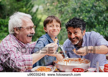 Stock Photography - Boy enjoying a meal together with father and grandfather. Fotosearch
