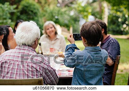 Stock Image - Boy photographing family at outdoor meal. Fotosearch