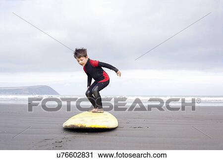 Stock Image - Boy practising on surfboard on beach. Fotosearch