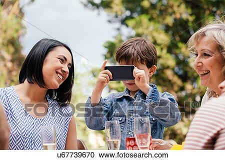 Boy taking a picture with phone at family event View Large Photo Image Stock Image - Boy taking a picture with phone at family event. Fotosearch