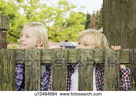 Picture - Brother and sister peering over wooden gate. Fotosearch