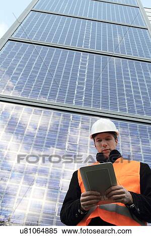 Stock Photography - Builder standing in front of skyscraper using digital tablet. Fotosearch