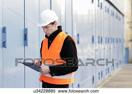 Stock Photography - Builder writing paperwork using clipboard. Fotosearch