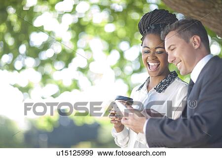 Businessman and business woman sharing message on cellular phone View Large Photo Image Stock Photo - Businessman and business woman sharing message on cellular phone. Fotosearch