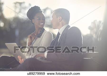 Businessman and business woman using laptop on park bench View Large Photo Image Stock Photo - Businessman and business woman using laptop on park bench. Fotosearch