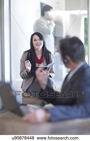 Stock Photo - Businessman using laptop, businesswoman writing. Fotosearch