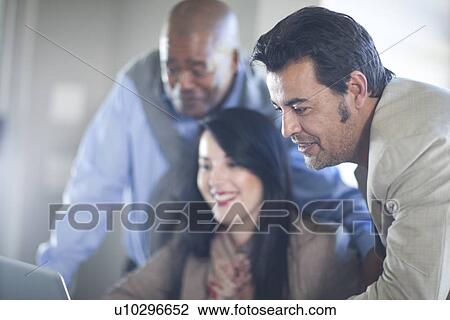 Stock Image - Businesspeople sitting around laptop. Fotosearch