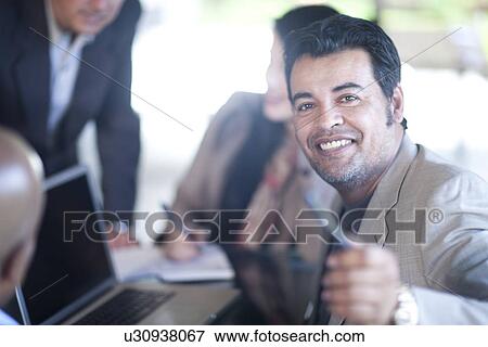 Stock Photo - Businesspeople sitting around laptop. Fotosearch