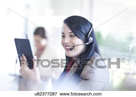 Stock Photo - Businesswoman using digital tablet and having telephone conversation on headset. Fotosearch