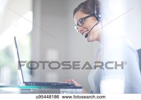 Stock Photograph - Businesswoman using laptop computer and telephone headset. Fotosearch