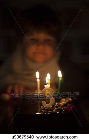 Stock Image - Candlelit male toddler looking at birthday cake. Fotosearch
