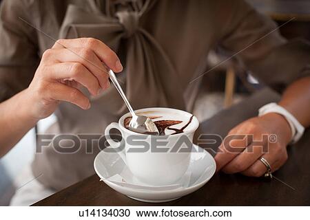 Stock Image - Close up of female hand stirring cappuccino. Fotosearch