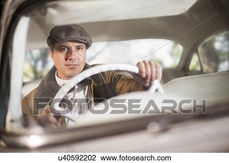 Stock Image - Close up of man in vintage car. Fotosearch