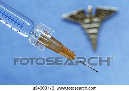 Stock Image - Close up of syringe with an out-of-focus caduceus in the background. Fotosearch