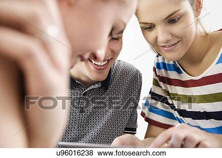 Stock Photo - Close up of three young adult friends looking at digital tablet. Fotosearch