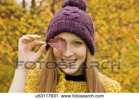 Close up of young woman in park holding autumn leaf over her eye View Large Photo Image Stock Image - Close up of young woman in park holding autumn leaf over her eye. Fotosearch