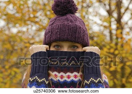 Stock Photograph - Close up portrait of young woman in park with jumper hiding face. Fotosearch