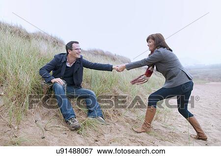 Stock Photo - Couple getting up from sand dune. Fotosearch