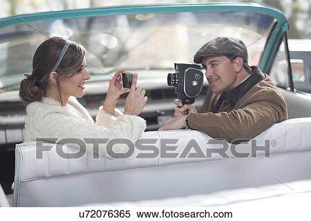 Couple in convertible filming and photographing each other with modern and vintage equipment View Large Photo Image Stock Photography - Couple in convertible filming and photographing each other with modern and vintage equipment. Fotosearch
