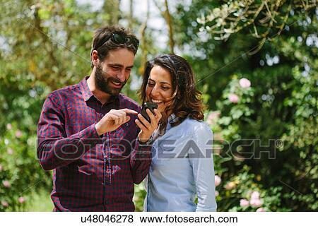 Stock Photo - Couple looking at mobile phone in park, Florence, Italy. Fotosearch