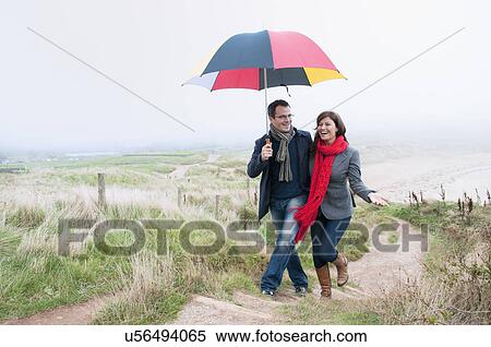 Couple on coast walk carrying umbrella, Thurlestone, Devon, UK View Large Photo Image Stock Photography - Couple on coast walk carrying umbrella, Thurlestone, Devon, UK. Fotosearch