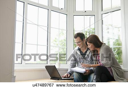 Couple on window seat, using laptop View Large Photo Image Stock Photo - Couple on window seat, using laptop. Fotosearch
