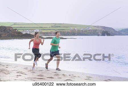 Stock Image - Couple running on beach, Thurlestone, Devon, UK. Fotosearch