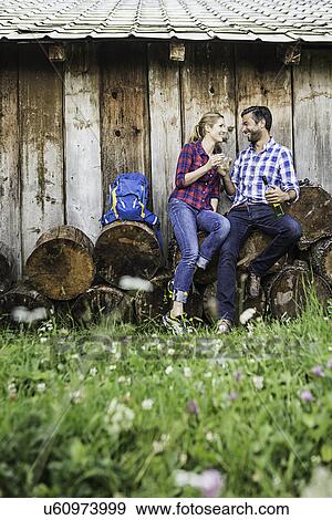 Couple sitting on cut logs having wine View Large Photo Image Stock Photo - Couple sitting on cut logs having wine. Fotosearch