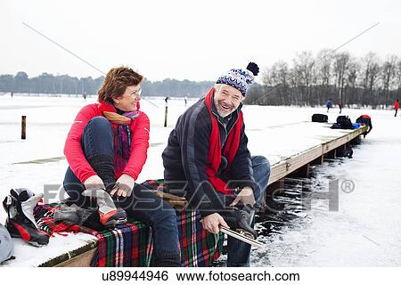 Couple sitting on pier putting on ice skates View Large Photo Image Stock Photograph - Couple sitting on pier putting on ice skates. Fotosearch