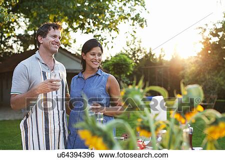Couple standing in garden, drinking glass of water View Large Photo Image Stock Photograph - Couple standing in garden, drinking glass of water. Fotosearch