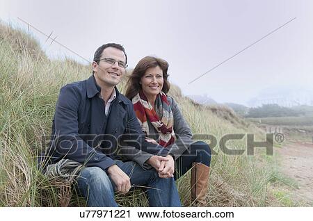 Stock Image - Couple watching from sand dune, Thurlestone, Devon, UK. Fotosearch