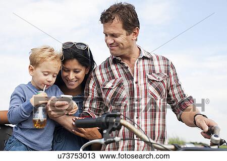 Stock Image - Family looking at smartphone and having a drink. Fotosearch