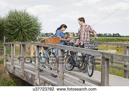 Stock Image - Family on bicycles on wood bridge, stopped for drink. Fotosearch