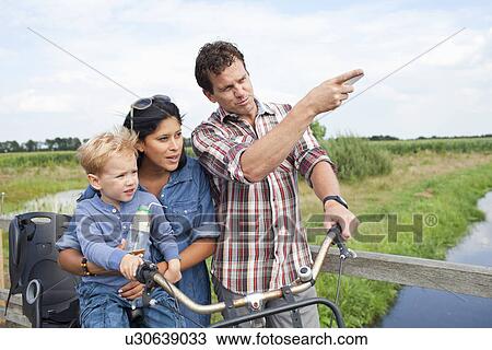 Stock Image - Family with bicycle, having drink, pointing. Fotosearch
