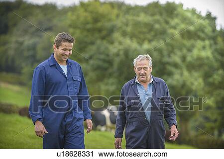 Stock Image - Farmer and son walking together in field. Fotosearch