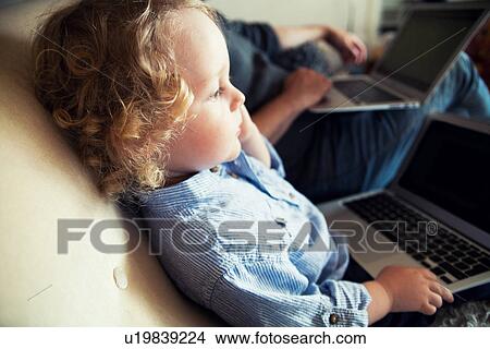 Picture - Father and male toddler on sofa with personal computers. Fotosearch