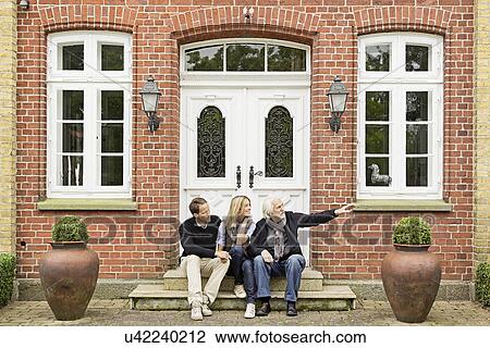 Stock Image - Father and mid adult couple sitting on doorstep. Fotosearch