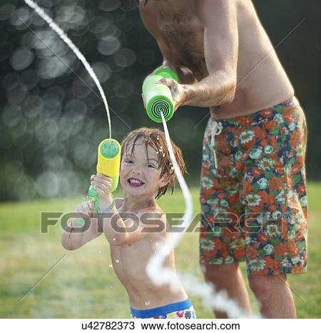 Stock Image - Father and son having fun with water gun. Fotosearch
