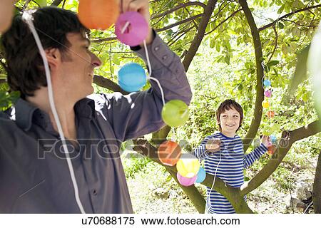 Stock Photography - Father and son putting fairy lights in tree. Fotosearch