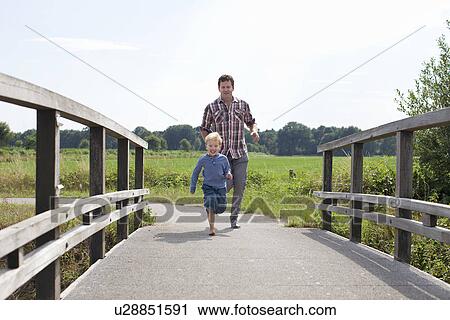 Stock Image - Father and son running over wooden bridge. Fotosearch