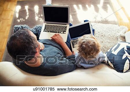 Stock Photography - Father and toddler son on sofa with personal computers. Fotosearch