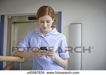 Picture - Female nurse looking at mobile phone outside hospital elevator. Fotosearch