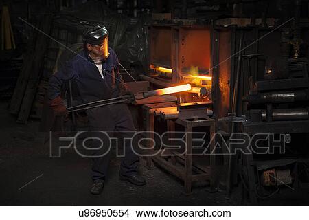 Picture - Forge worker pre heating steel billet for forging in upsetter. Fotosearch