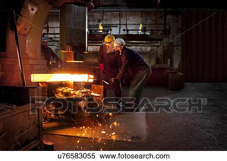 Stock Photography - Forge workers pre form red hot billet into flight bar (mining component) on hammer. Fotosearch