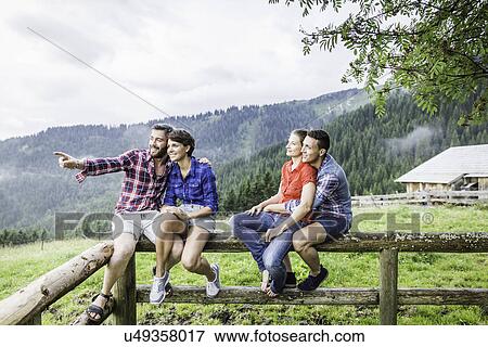 Stock Photo - Four friends sitting on fence, Tyrol Austria. Fotosearch