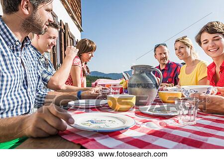 Stock Image - Friends sitting for breakfast outside chalet, Tyrol, Austria. Fotosearch