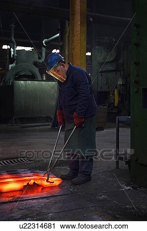 Stock Image - Fully forged and clipped flight bar (mining component) is lined up to cool down for final stage of finishing process. Fotosearch